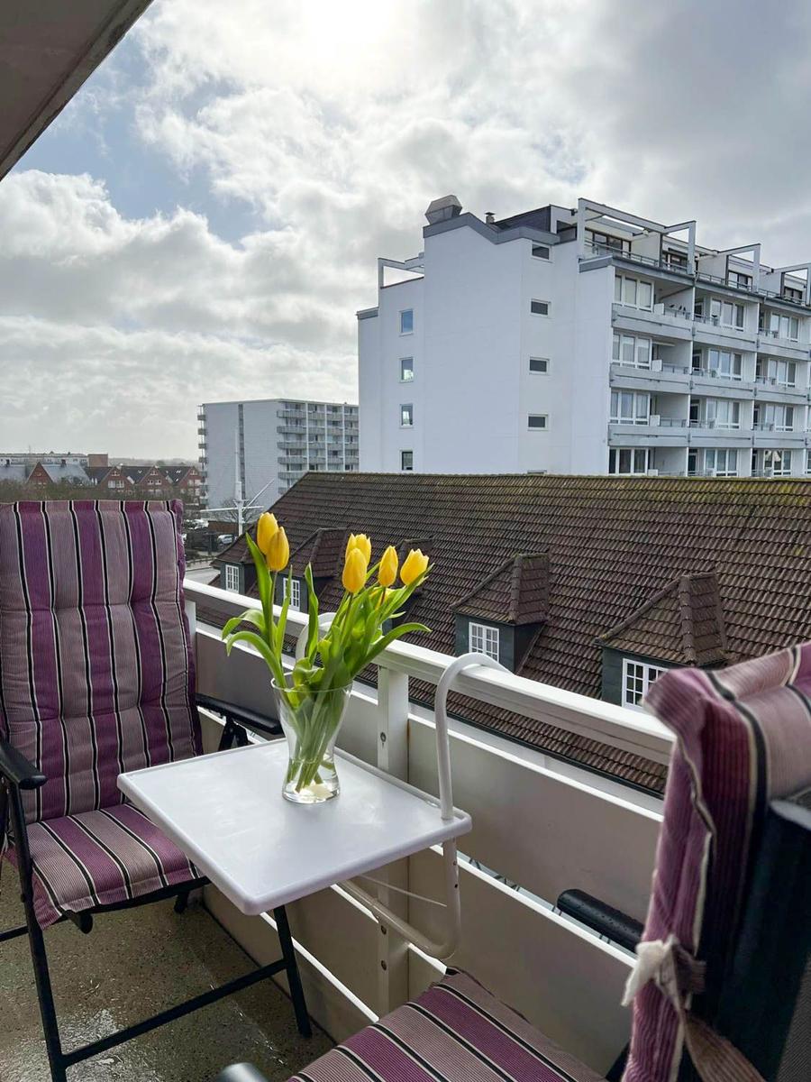 Balkon mit Stuhl, Tisch und Tulpenblumen. Blick auf Gebäude und Dächer.