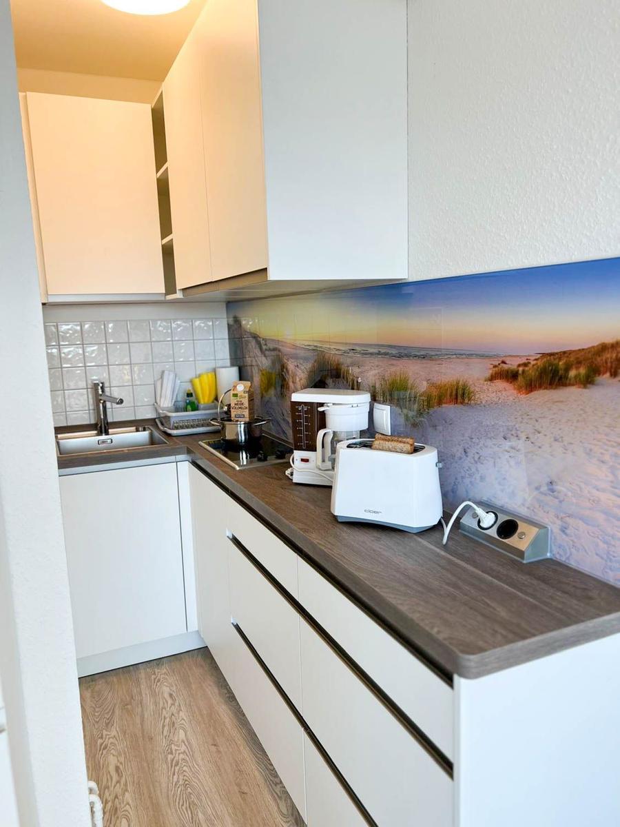 Küche mit weißen Schränken, Holzoptik Arbeitsplatte und Strandbild hinter dem Herd.