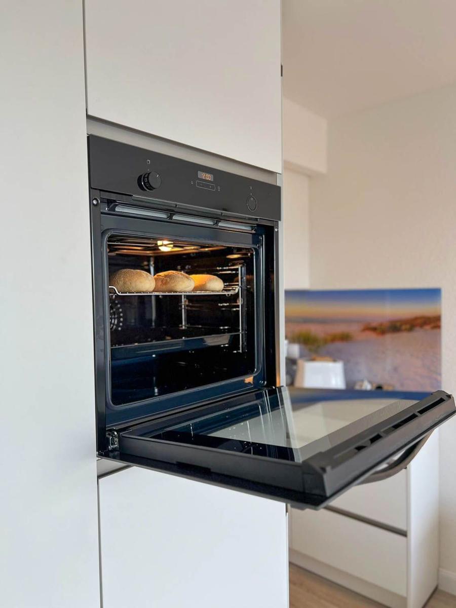 Eingebaute Dunstabzugshaube mit offenem Ofen und Brot im Backofen.