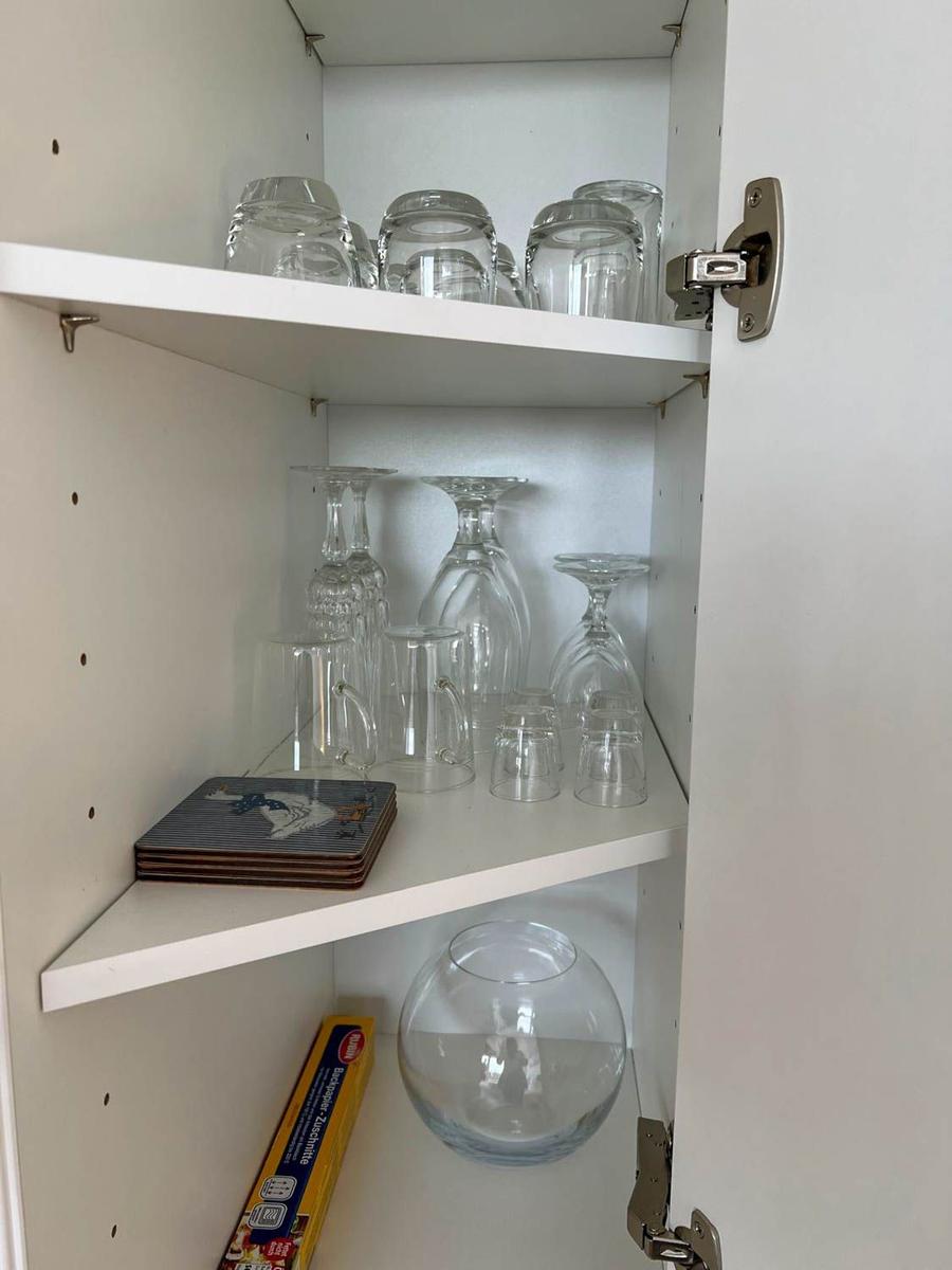 Weißer Schrank mit Gläsern und einem Glasbehälter auf den Regalen.