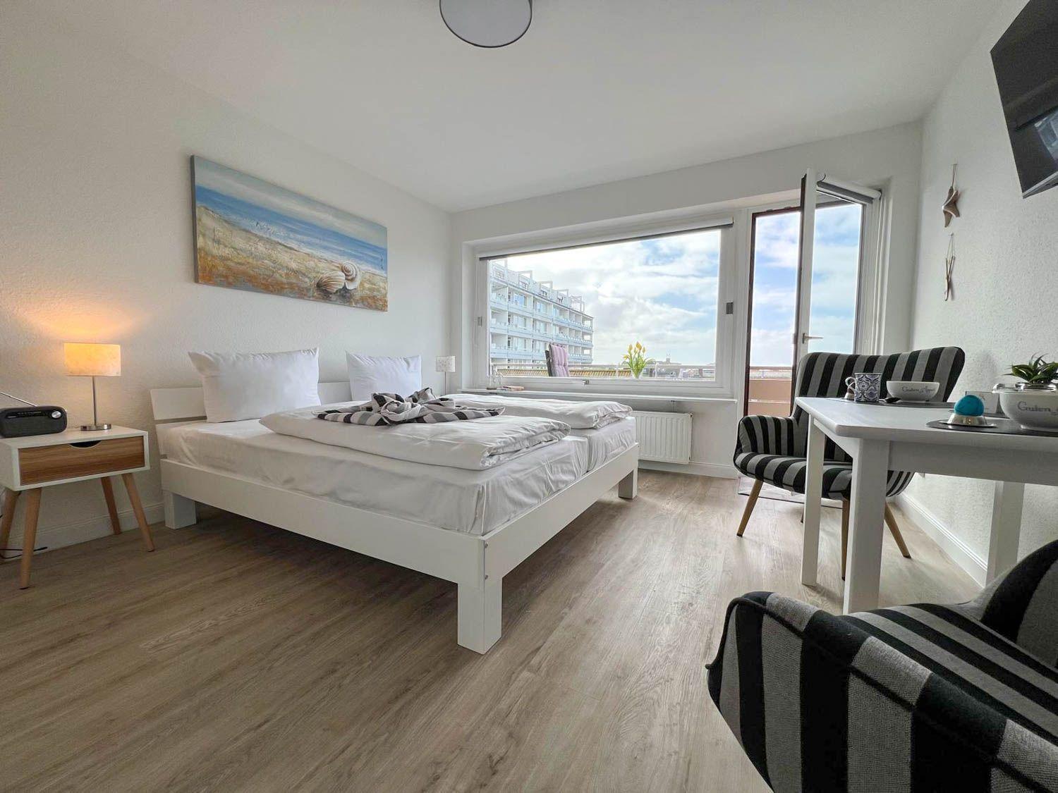 Schlafzimmer mit Bett, Tisch und Stühlen. Fenster mit Blick auf Gebäude.