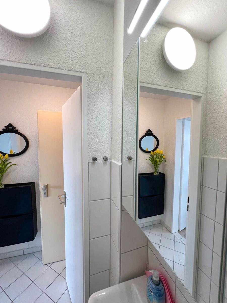 Badezimmer mit Spiegel, Waschbecken und dunklem Schrank. Gelbe Blumen auf dem Schrank.