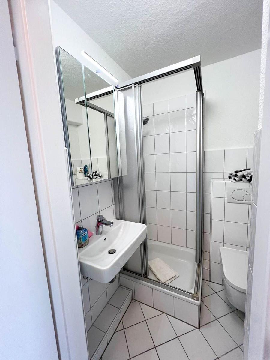 Badezimmer mit Dusche, Waschbecken und Toilette. Weiße Fliesen und Spiegelschrank.