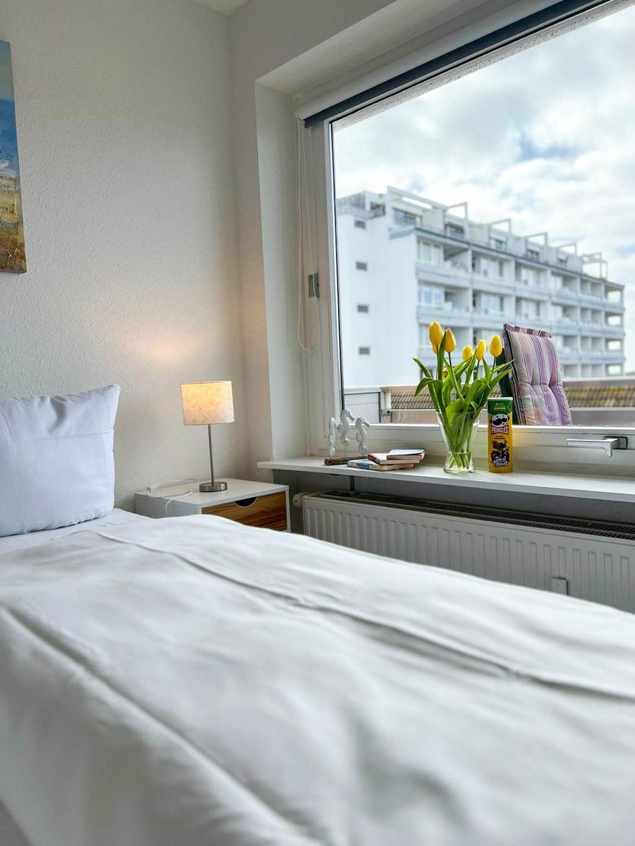 Schlafzimmer mit Bett, Nachttisch und Fensterblick auf Gebäude
