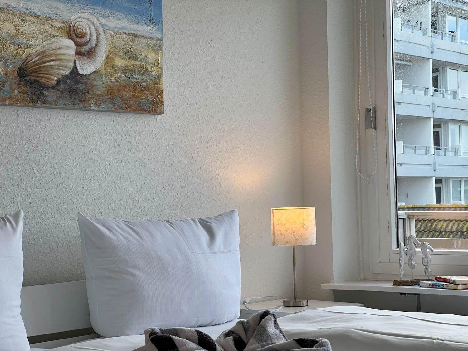 Schlafzimmer mit Bett, Wandbild und Lampe. Fenster zeigt Gebäude.