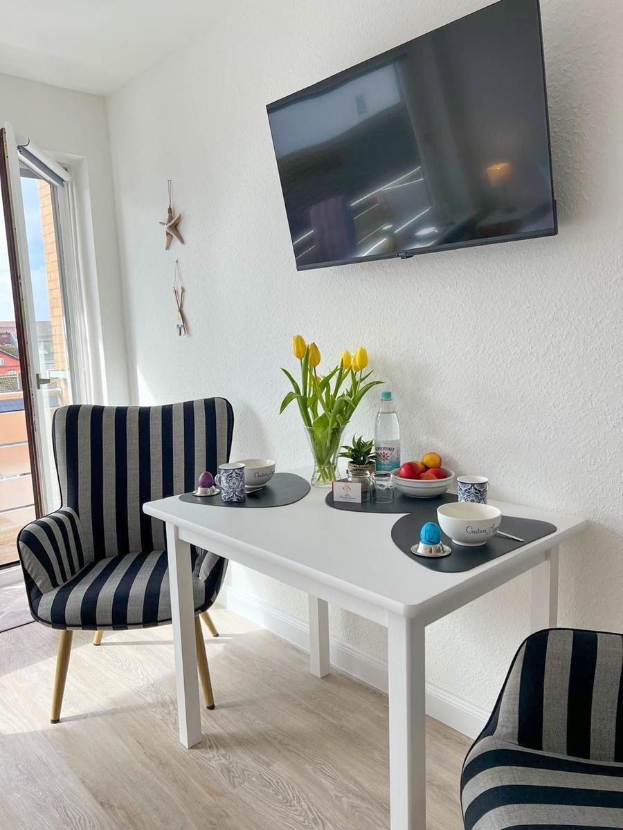 Esstisch mit zwei Stühlen, Fernseher und Blumen auf dem Tisch.