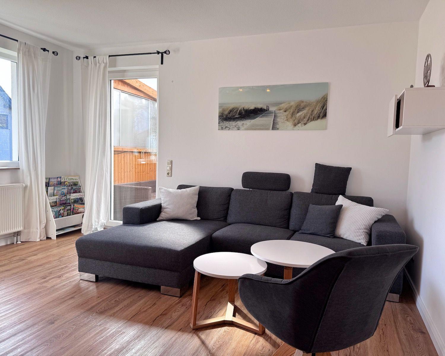 Ein Wohnzimmer mit grauem Sofa, zwei runden Tischen und einem Bild an der Wand.