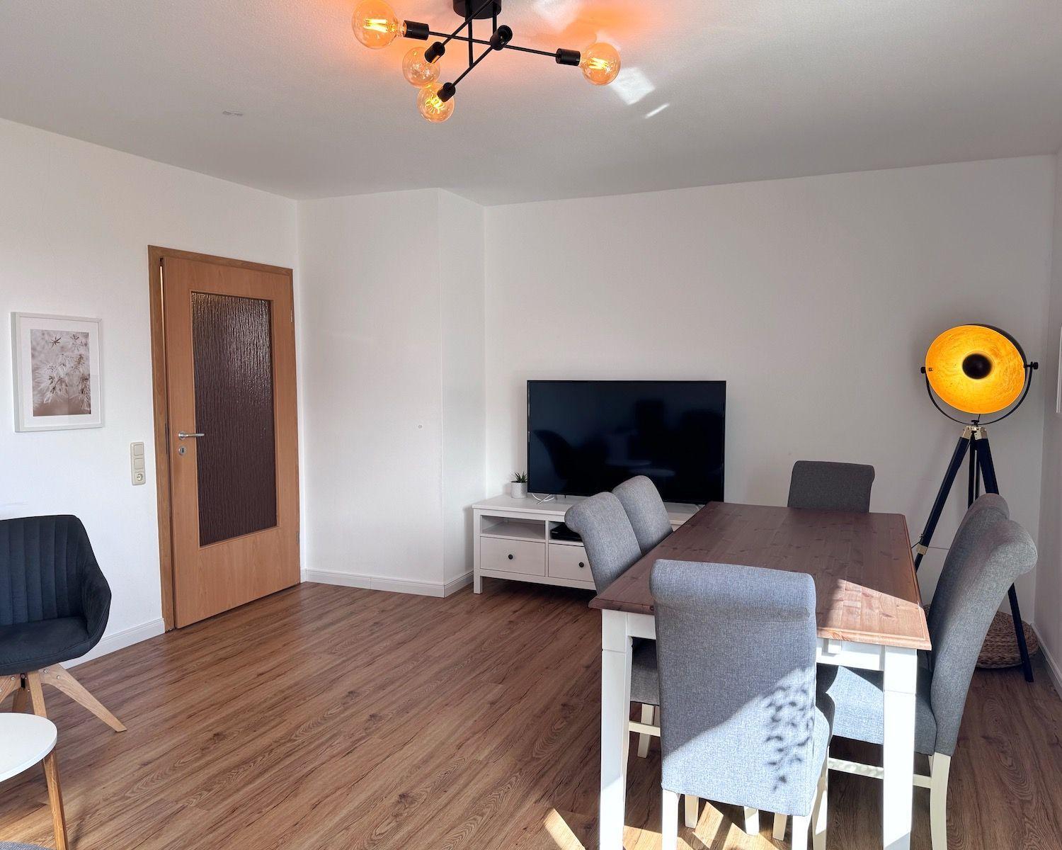 Essbereich mit Tisch, Stühlen und Fernseher. Holzboden und moderne Beleuchtung.