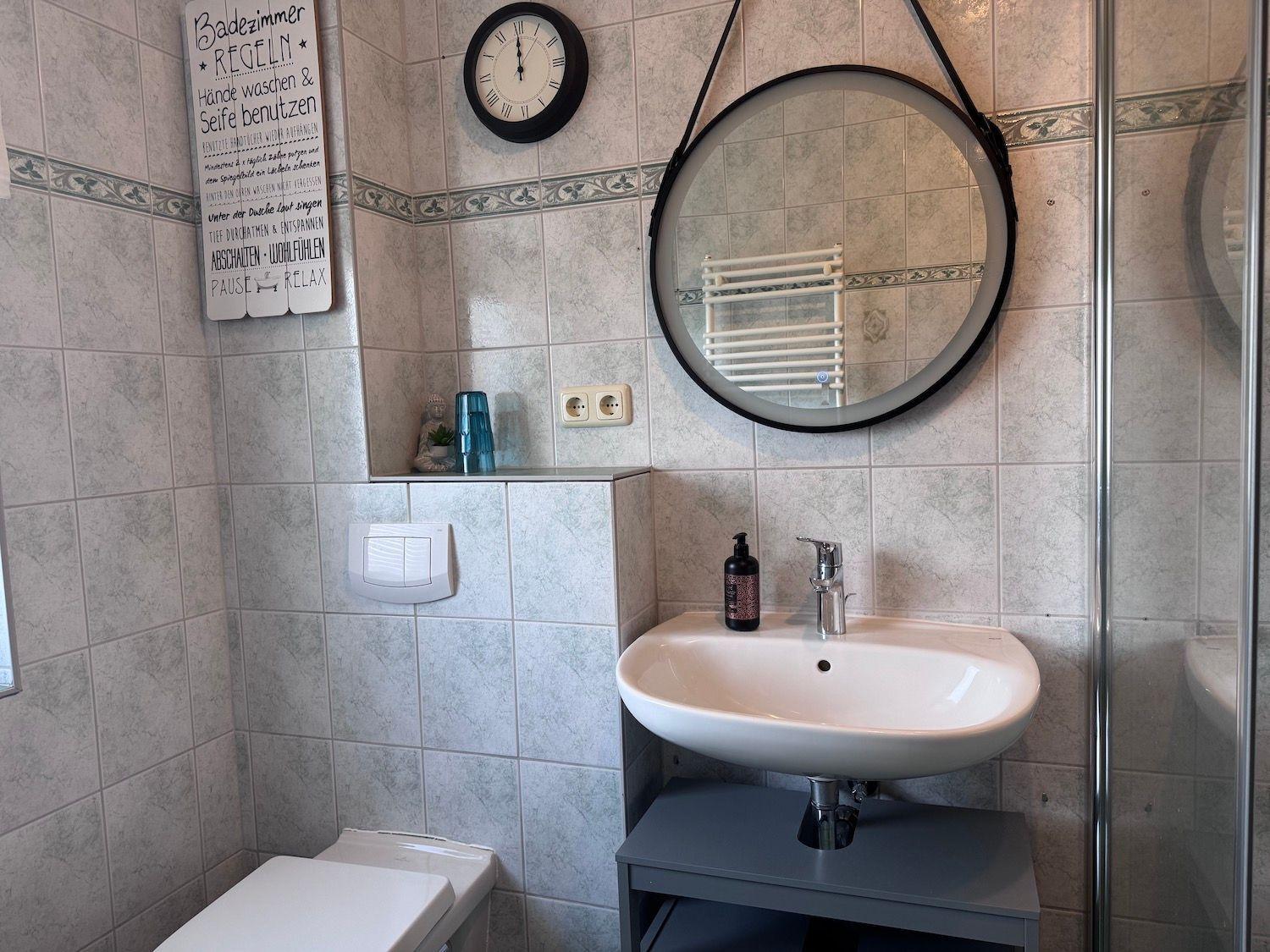 Badezimmer mit Waschbecken, Spiegel, Toilette und Dusche.