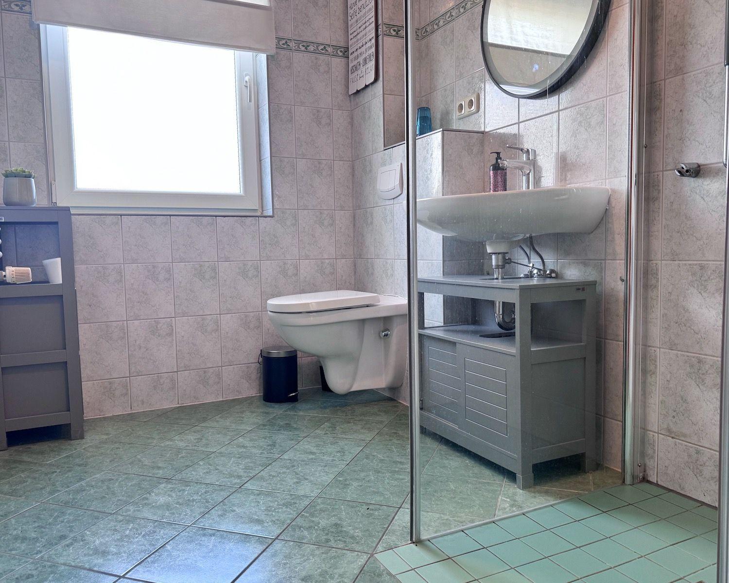 Badezimmer mit Toilette, Waschbecken und Dusche. Fliesenboden und Wandfliesen.