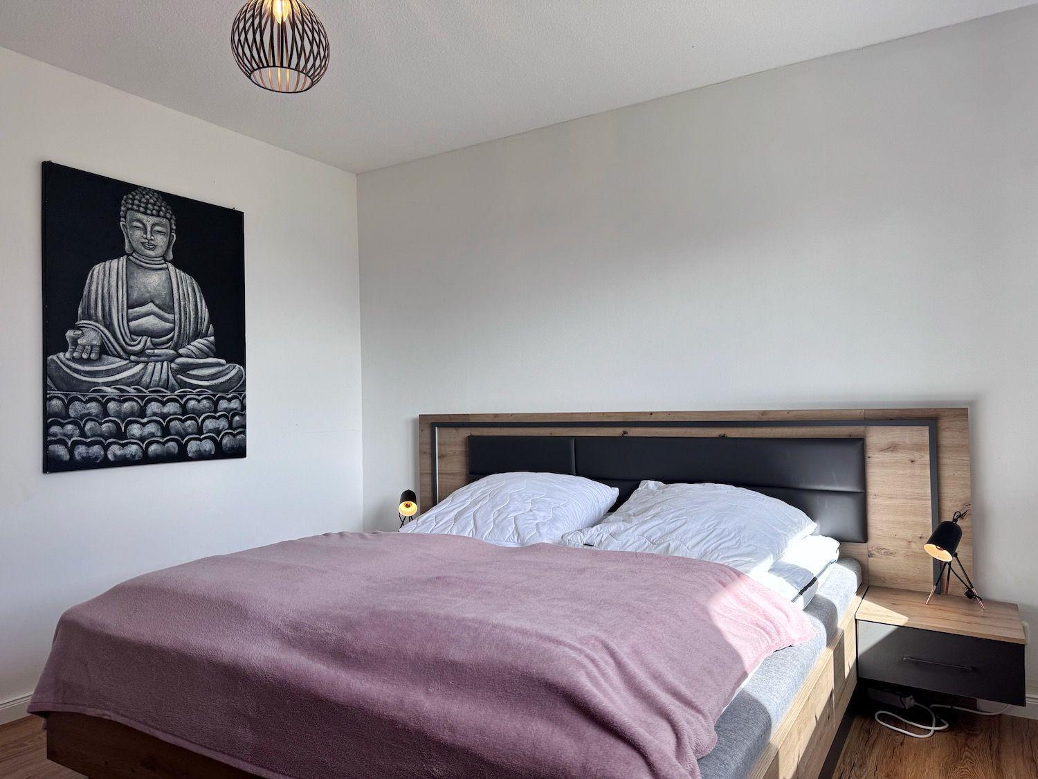 Schlafzimmer mit Bett, Nachttisch und Buddha-Bild an der Wand.
