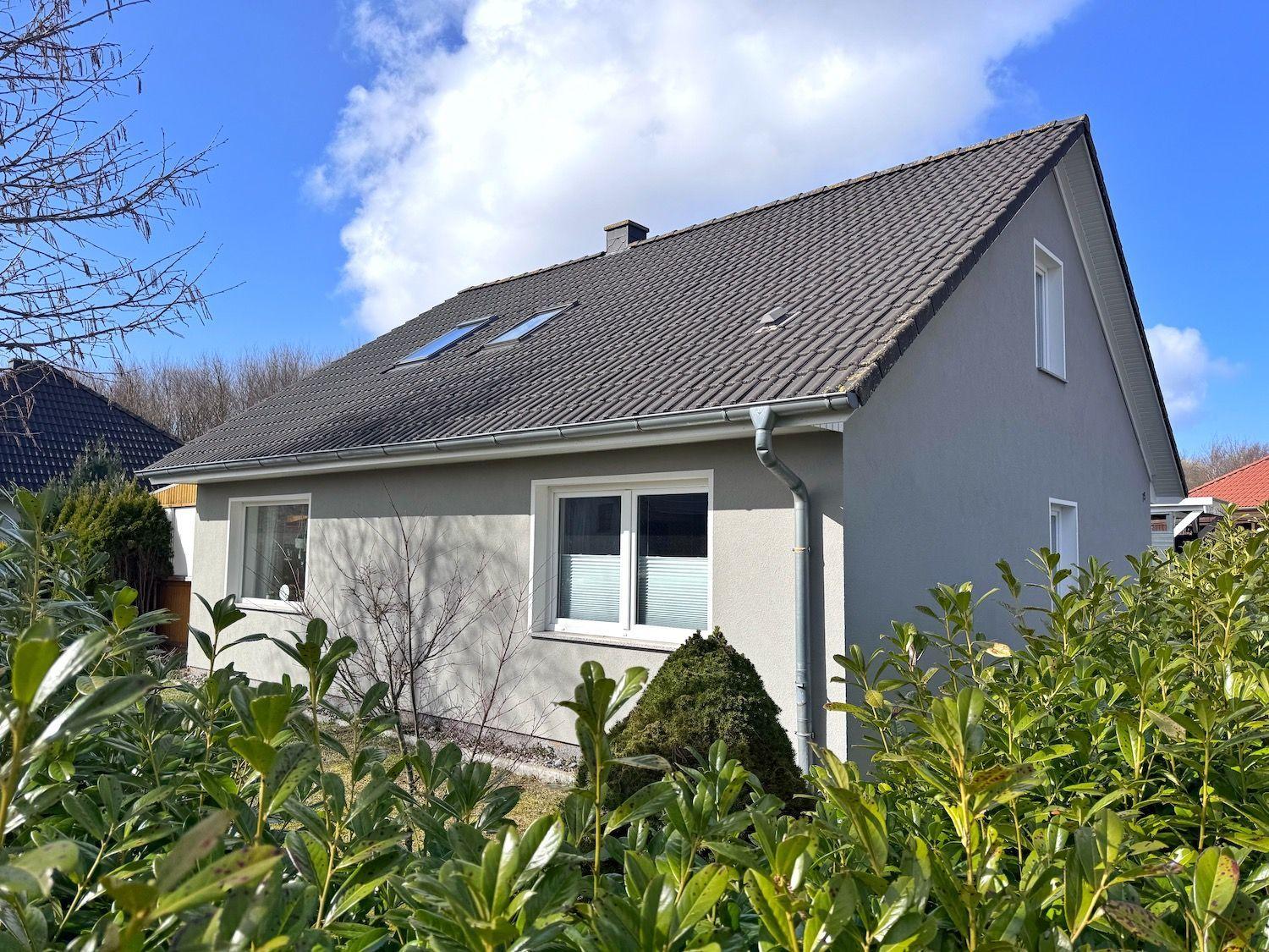 Ein Haus mit grauer Fassade, Dach mit Dachfenstern und grüner Umgebung.