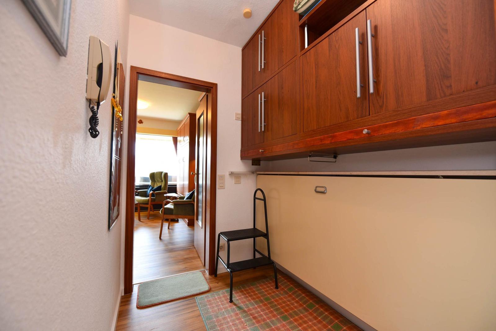 Flur mit Holzschrank, Treppenstufe und Blick in Wohnzimmer.