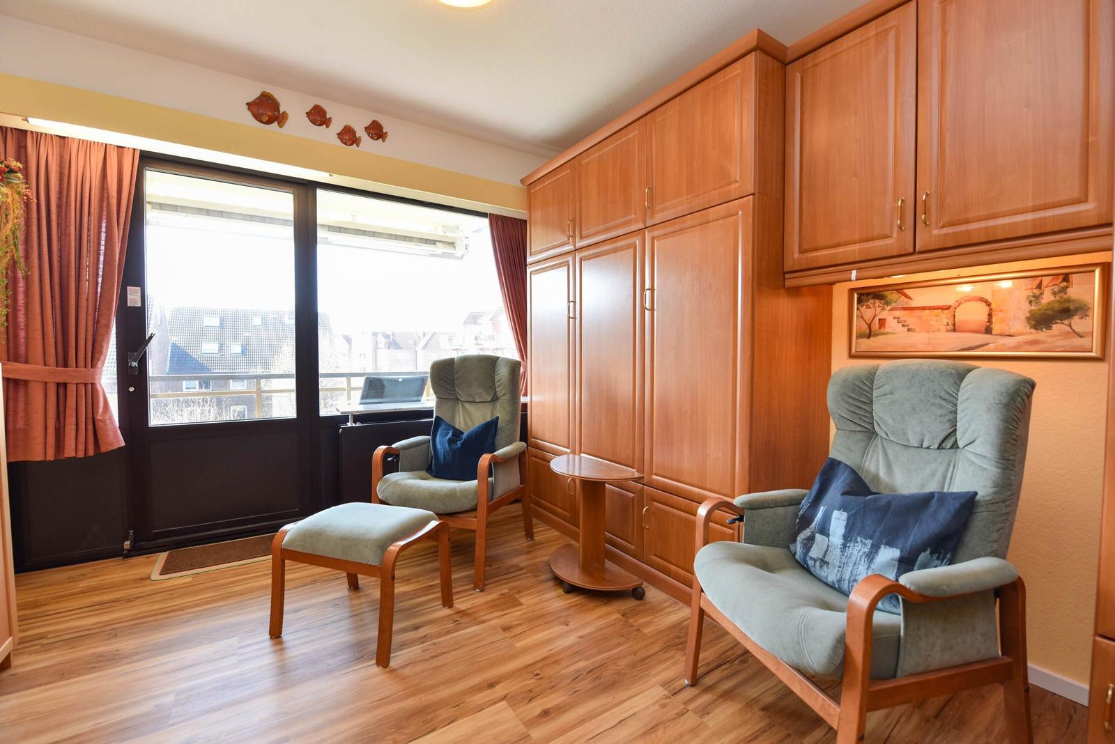 Zimmer mit Holzmöbeln, zwei Sesseln und Blick auf Balkon.