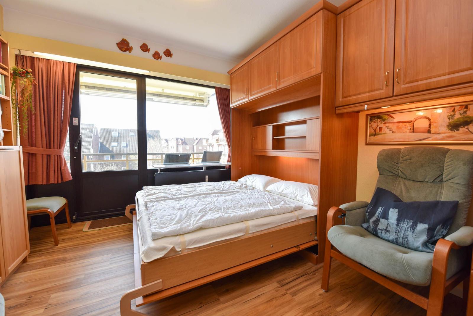 Schlafzimmer mit Bett, Sessel und Fenster zum Balkon