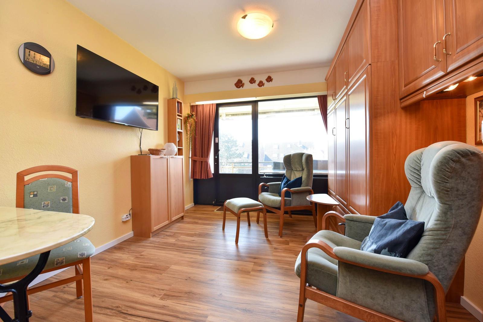 Wohnzimmer mit TV, Sitzgelegenheiten und Fenster zum Balkon.
