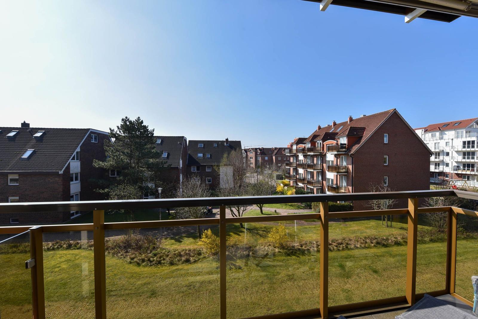 Balkon mit Blick auf Wohnhäuser und Grünflächen unter blauem Himmel.