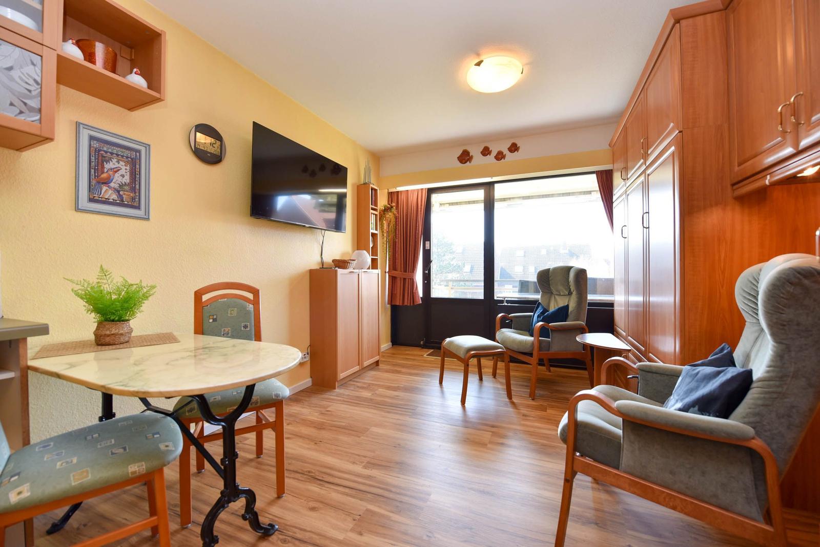 Wohnzimmer mit Essbereich, Fernseher und großem Fenster. Holzmöbel und Parkettboden.