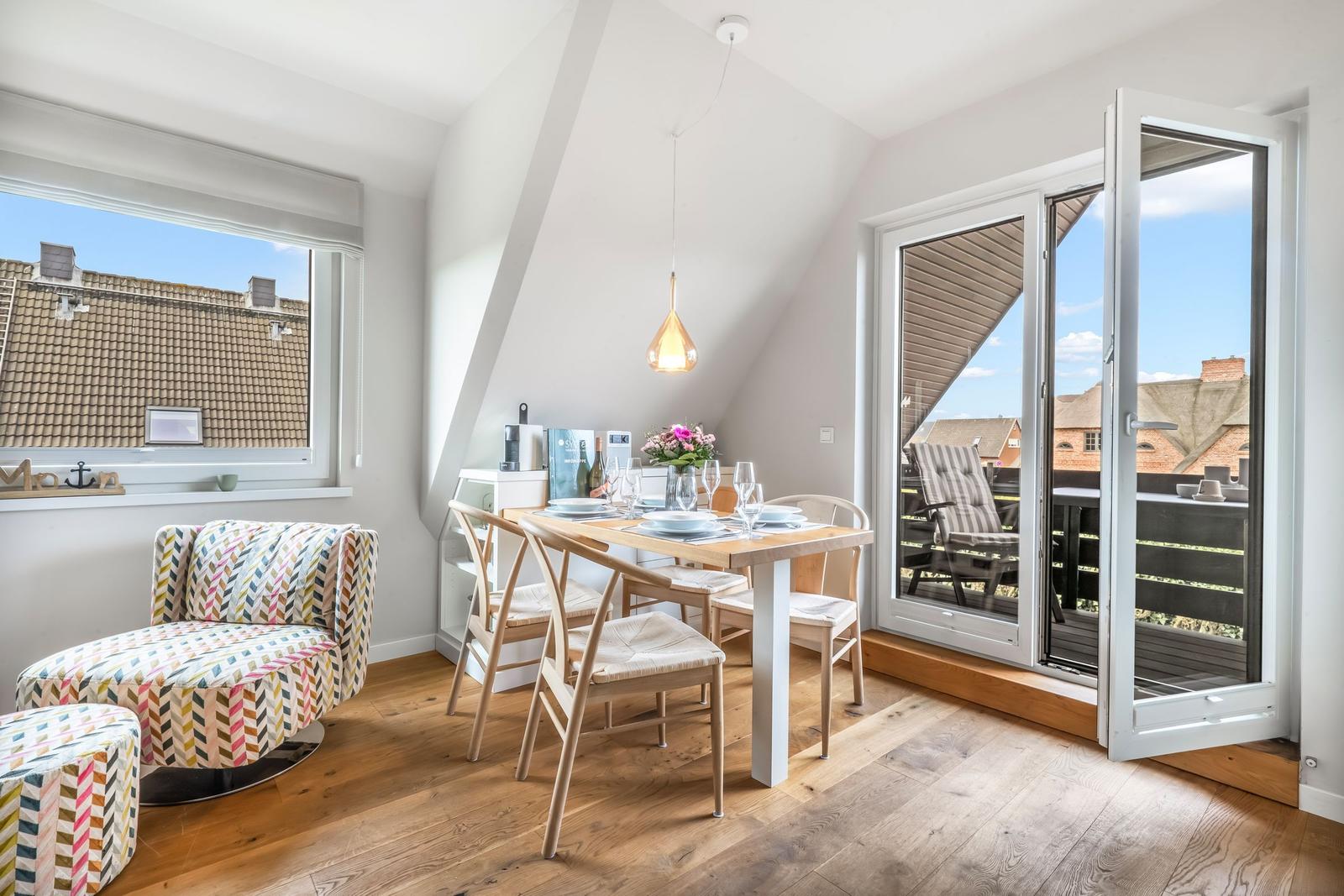 Dining room with table, chairs, and balcony access. Wooden floor and large window.
