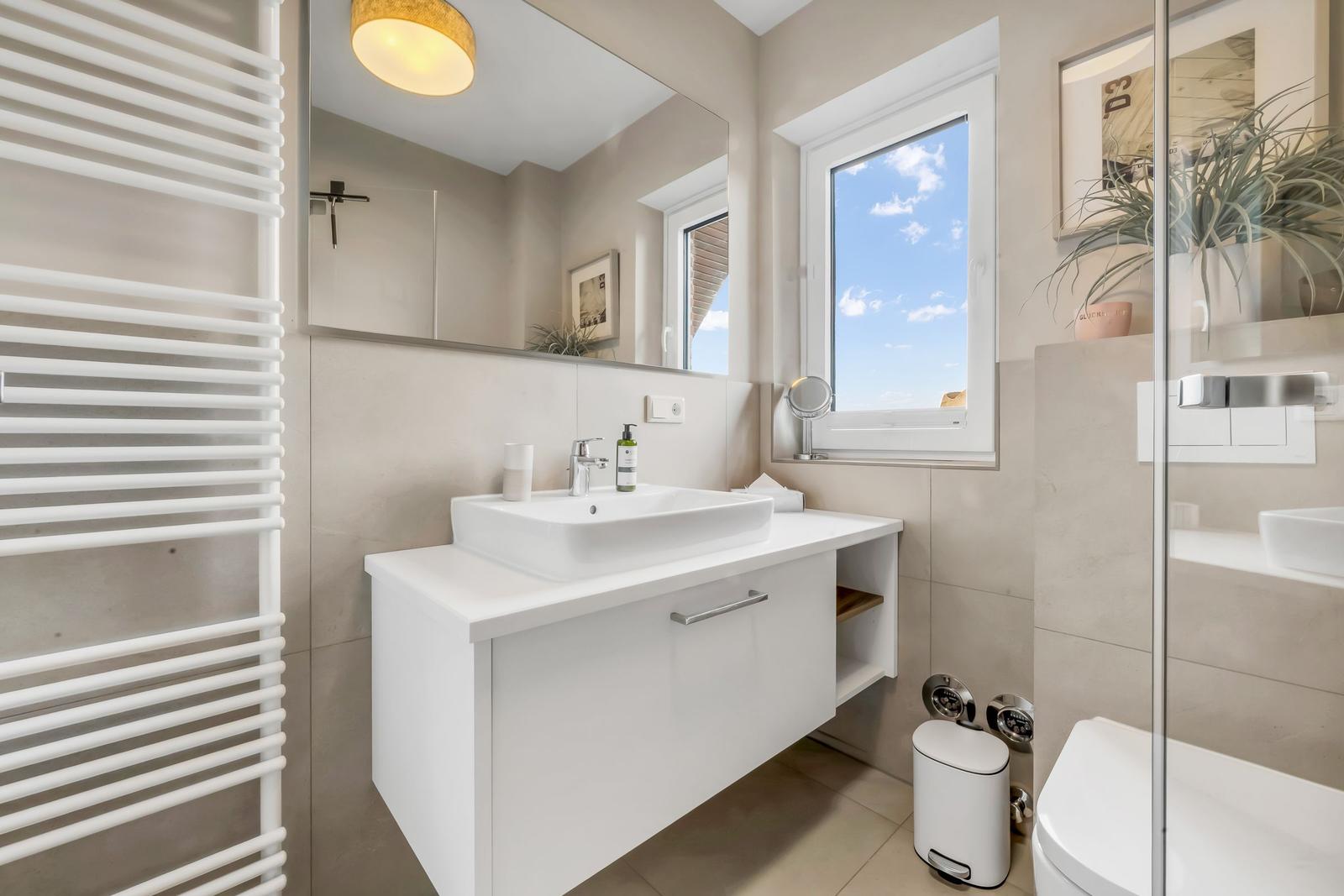 Bathroom with sink, mirror, window, and shower.