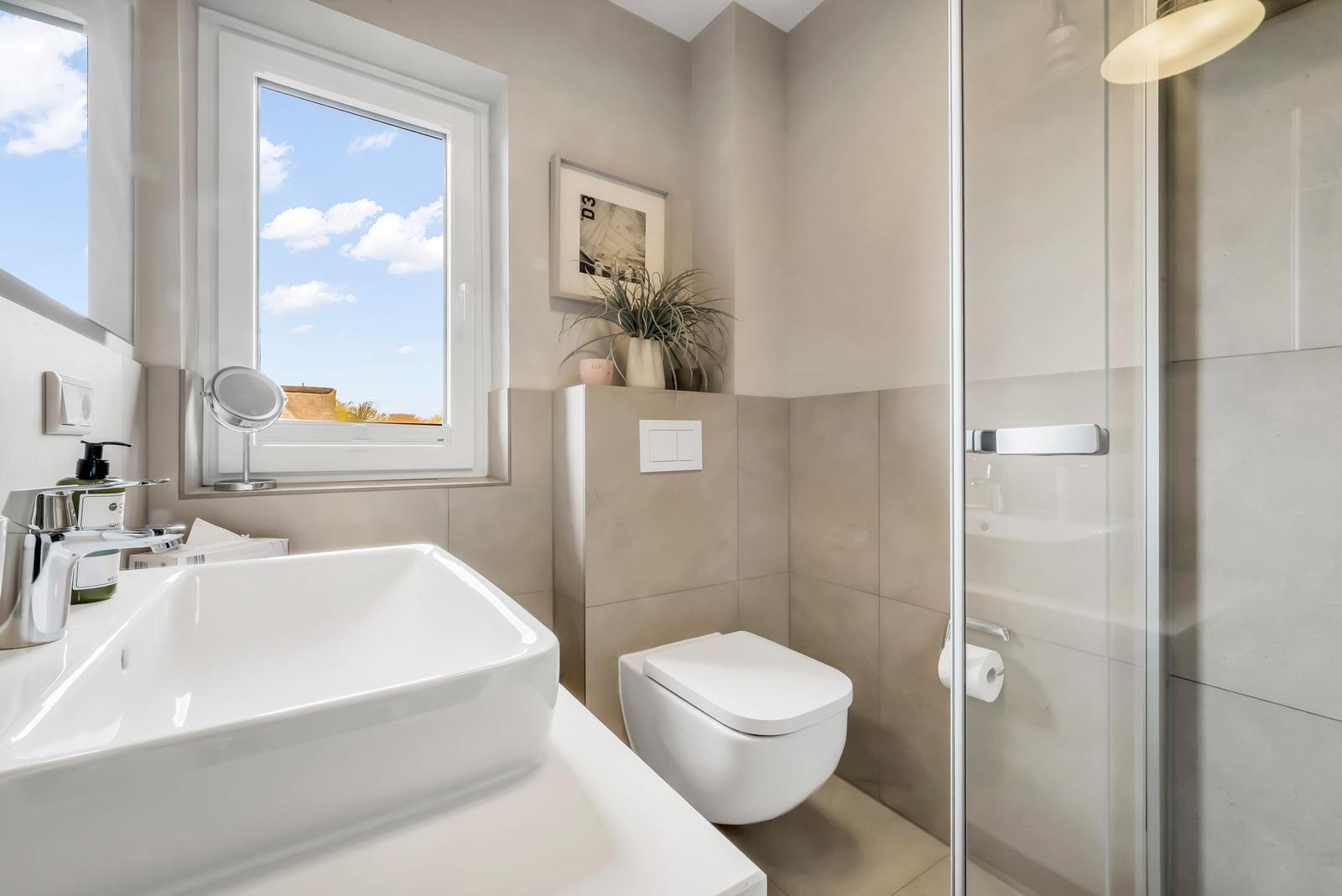 Bathroom with sink, toilet, and shower. Window with view of the sky.