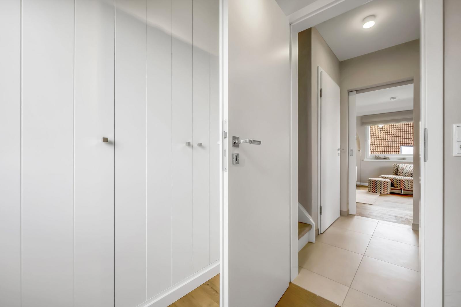 Hallway with white closets and door to living room with sofa.