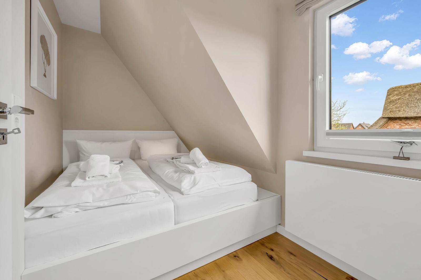 Room with two beds under sloped ceiling and large window with view of roof