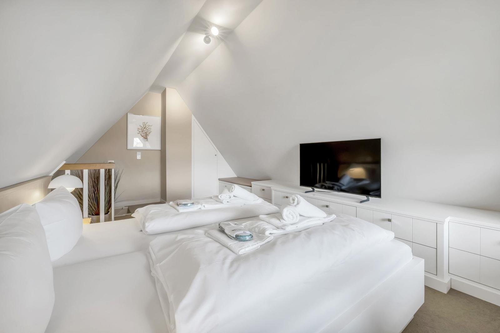 Bedroom with sloped ceiling, bed, TV, and dresser.