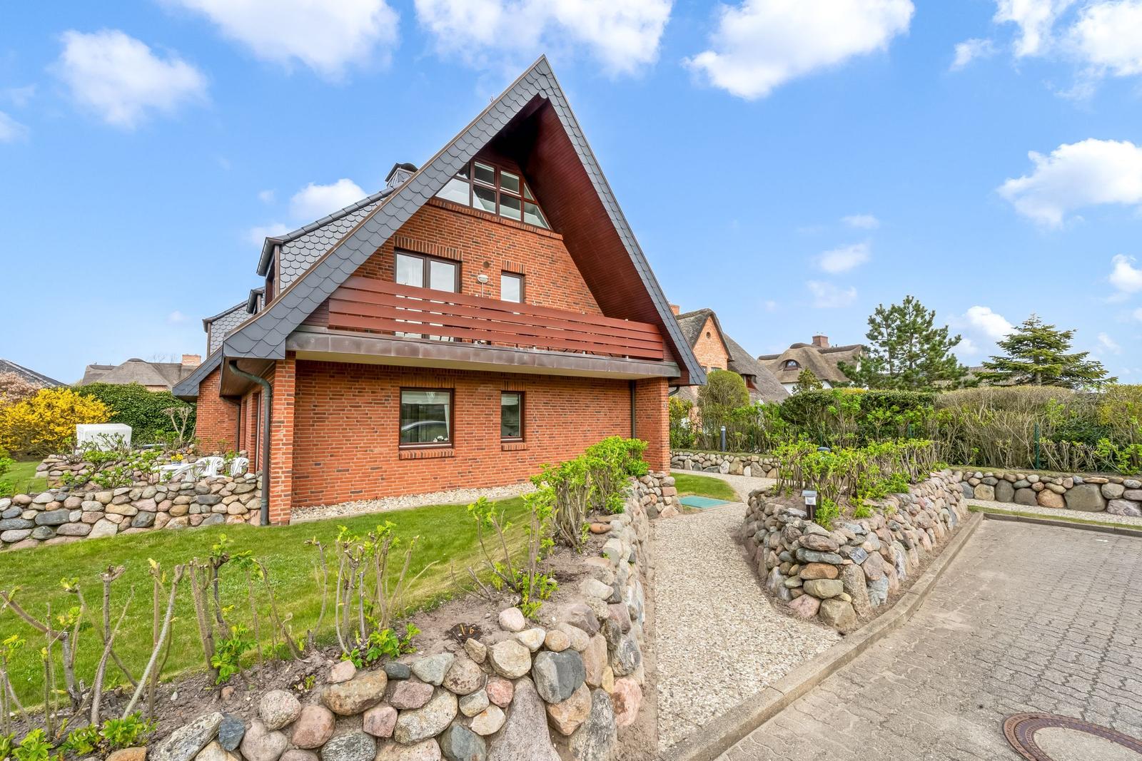 Red brick house with balcony and stone wall in the garden.