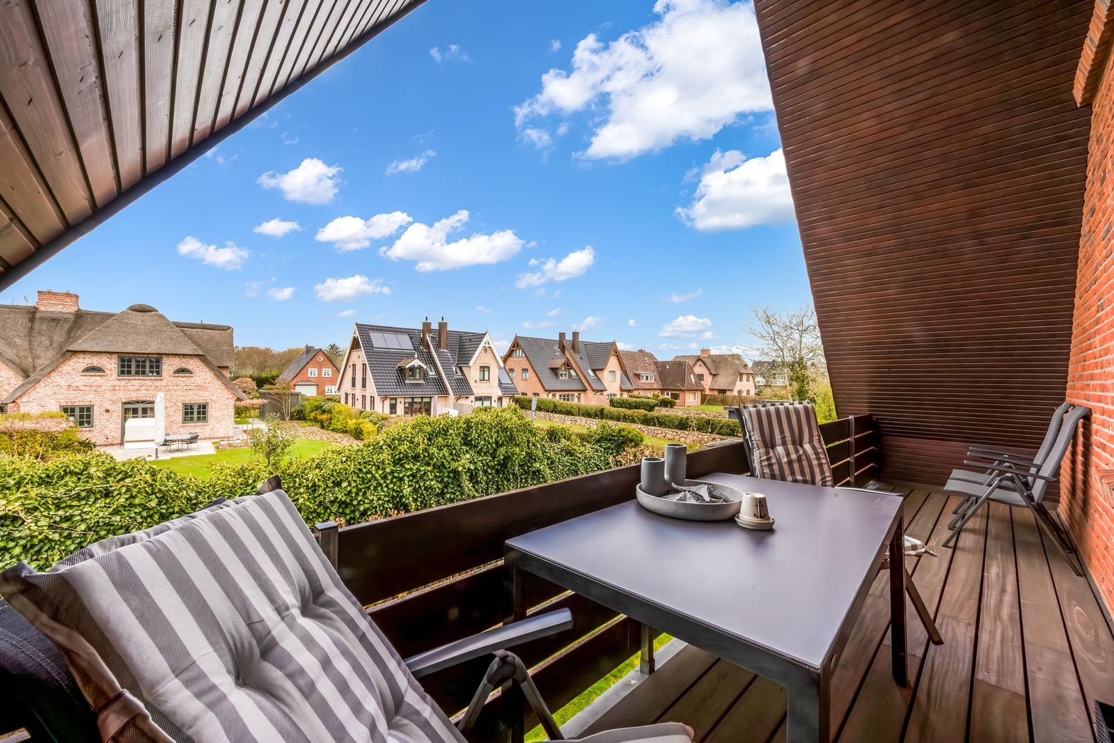 Terrace with table and chairs, view of houses and green areas under blue sky.