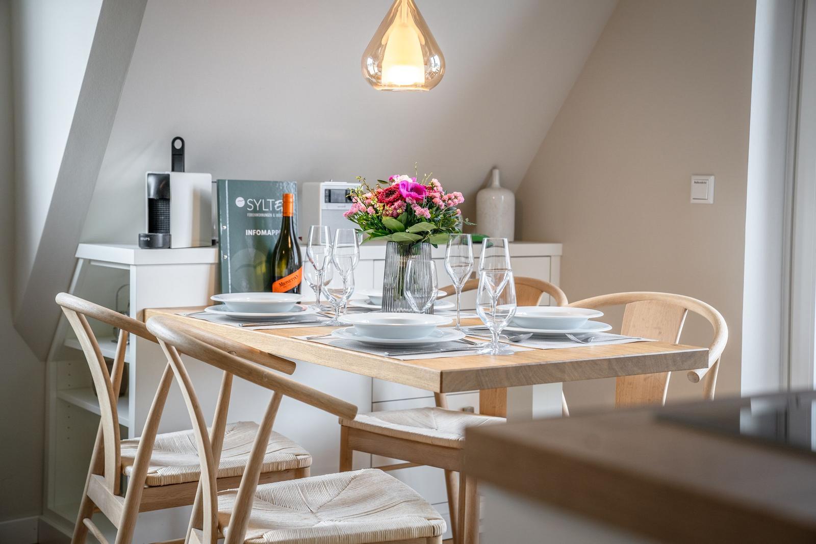 Dining table with four chairs, flowers, and glasses under a pendant light.