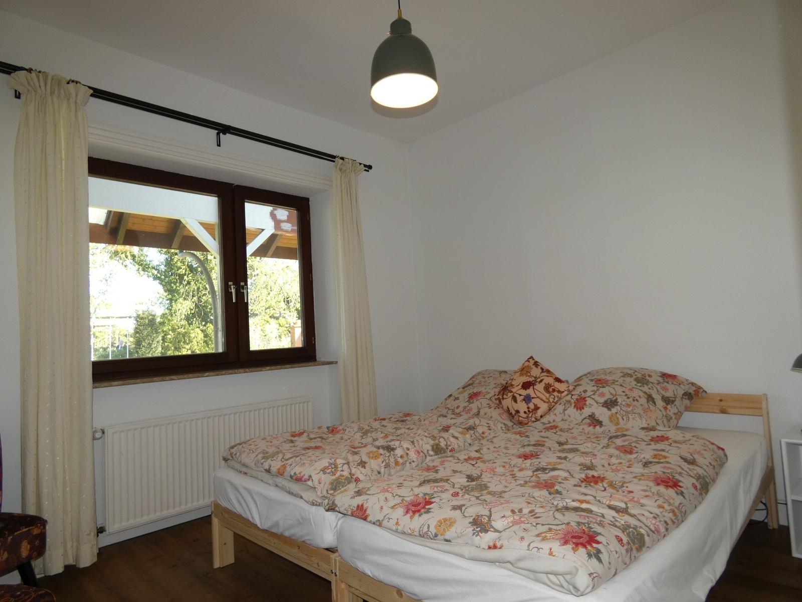 Schlafzimmer mit Doppelbett, Fenster und Deckenleuchte.