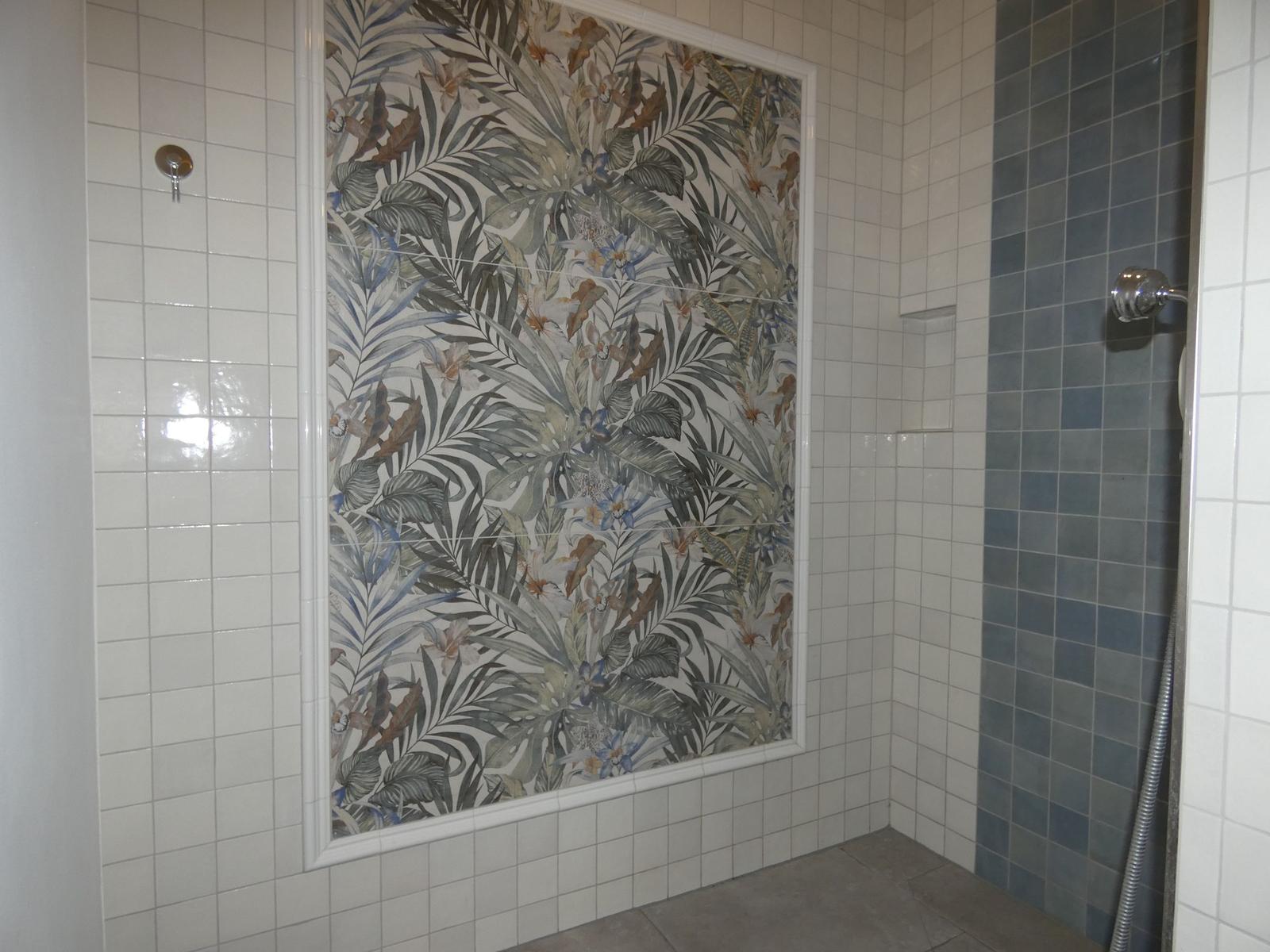 Duschbereich mit floraler Fliesenwand und weißen sowie blauen Fliesen.