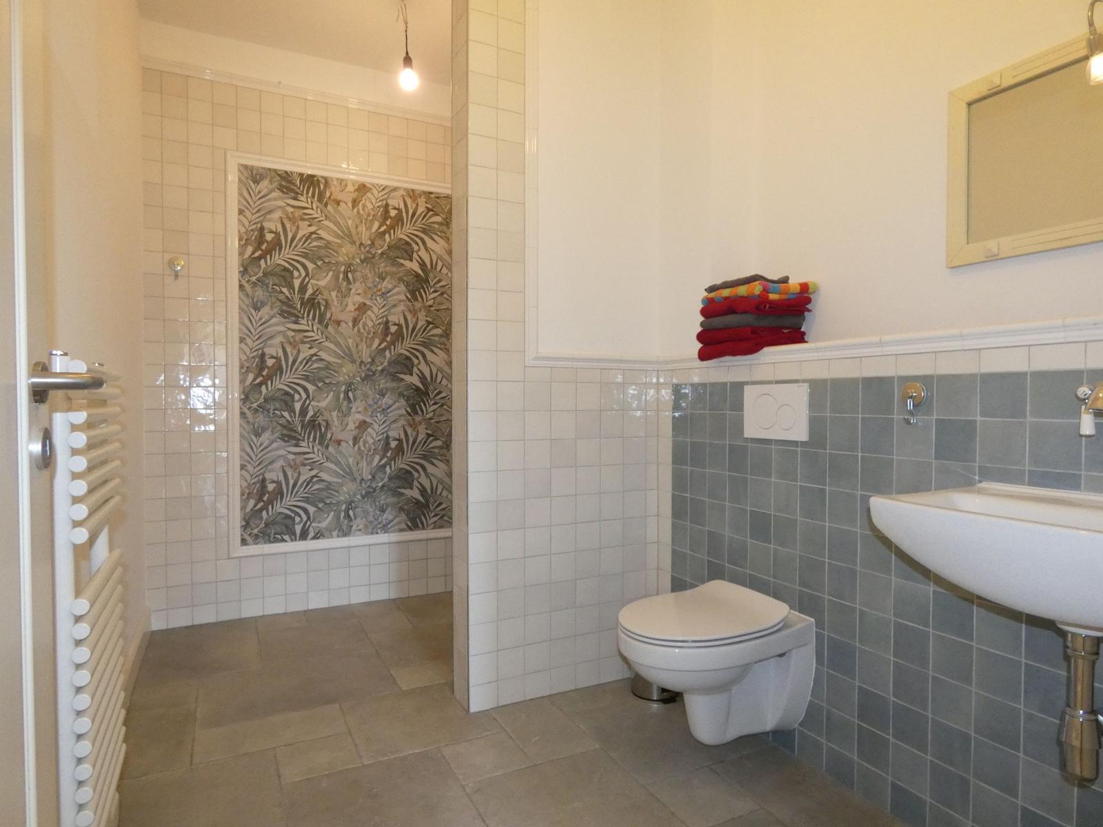 Badezimmer mit Dusche, Toilette und Waschbecken. Wand mit tropischen Motiv.