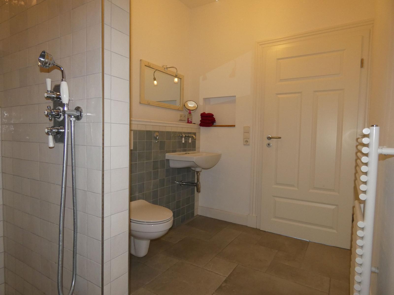 Bad mit Dusche, Waschbecken und Toilette. Weiße Wände, graue Fliesen.