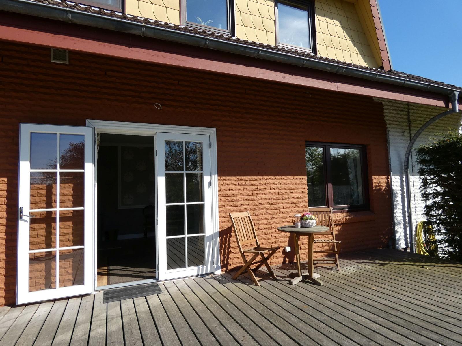 Terrasse mit Holztisch und Stühlen, Schiebetür zum Haus, rote Backsteinwand.