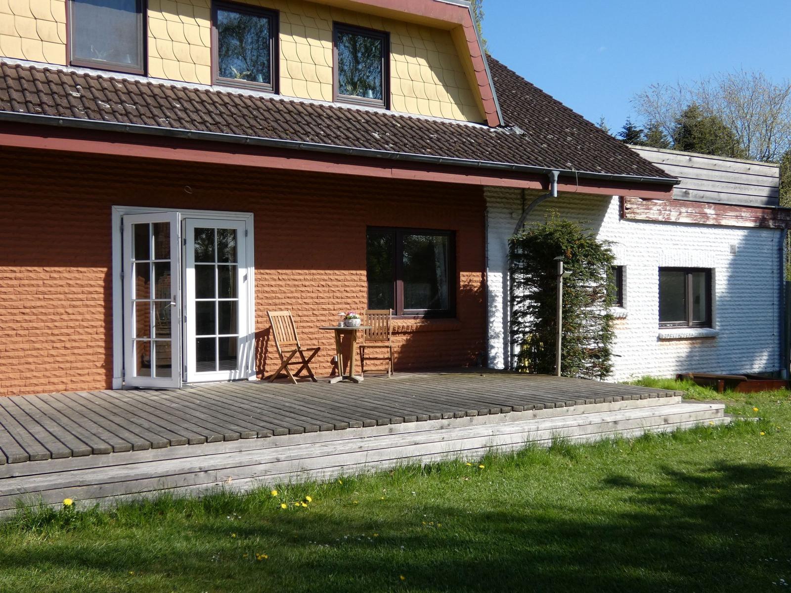 Haus mit Terrasse, Holzbank und Tisch. Fenster und Tür sind sichtbar.