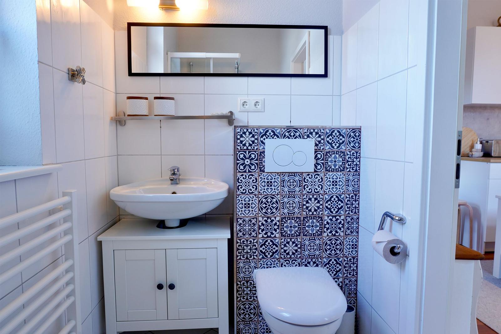 Badezimmer mit Waschbecken, Spiegel und Toilette mit blau-weißen Fliesen.