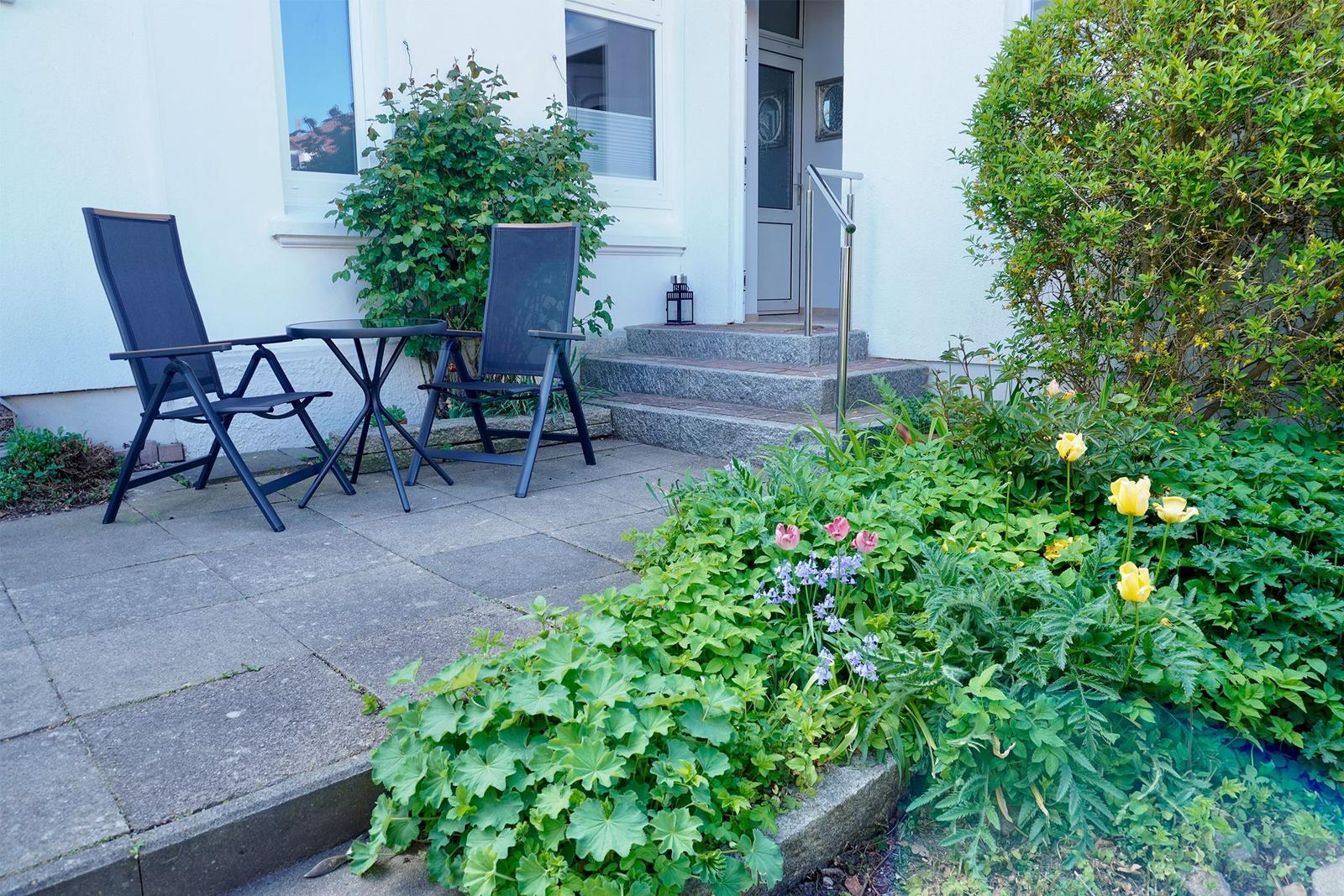 Terrasse mit zwei Stühlen und Tisch vor weißer Fassade mit Blumenbeet