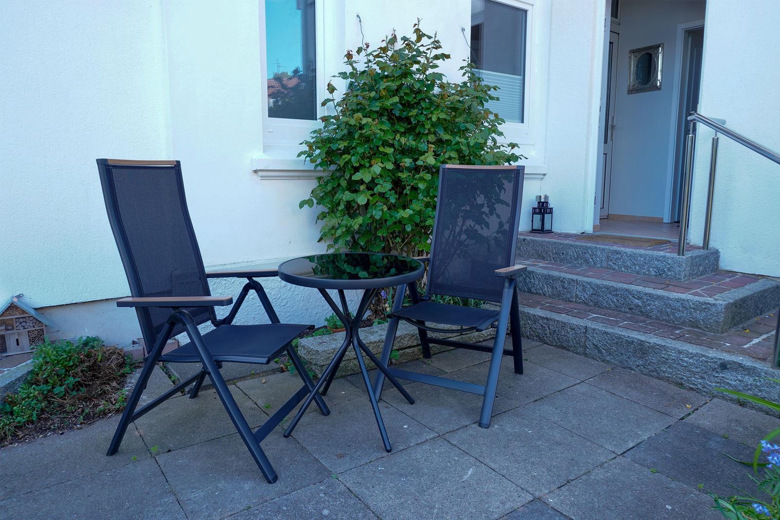 Zwei Stühle und ein Tisch auf der Terrasse vor dem Eingang.