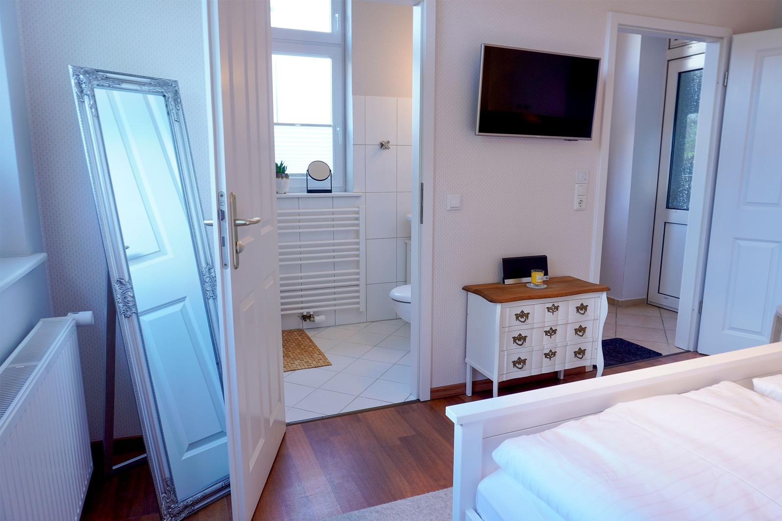 Schlafzimmer mit Bett, Schrank und Fernseher. Tür führt in Bad mit Toilette.