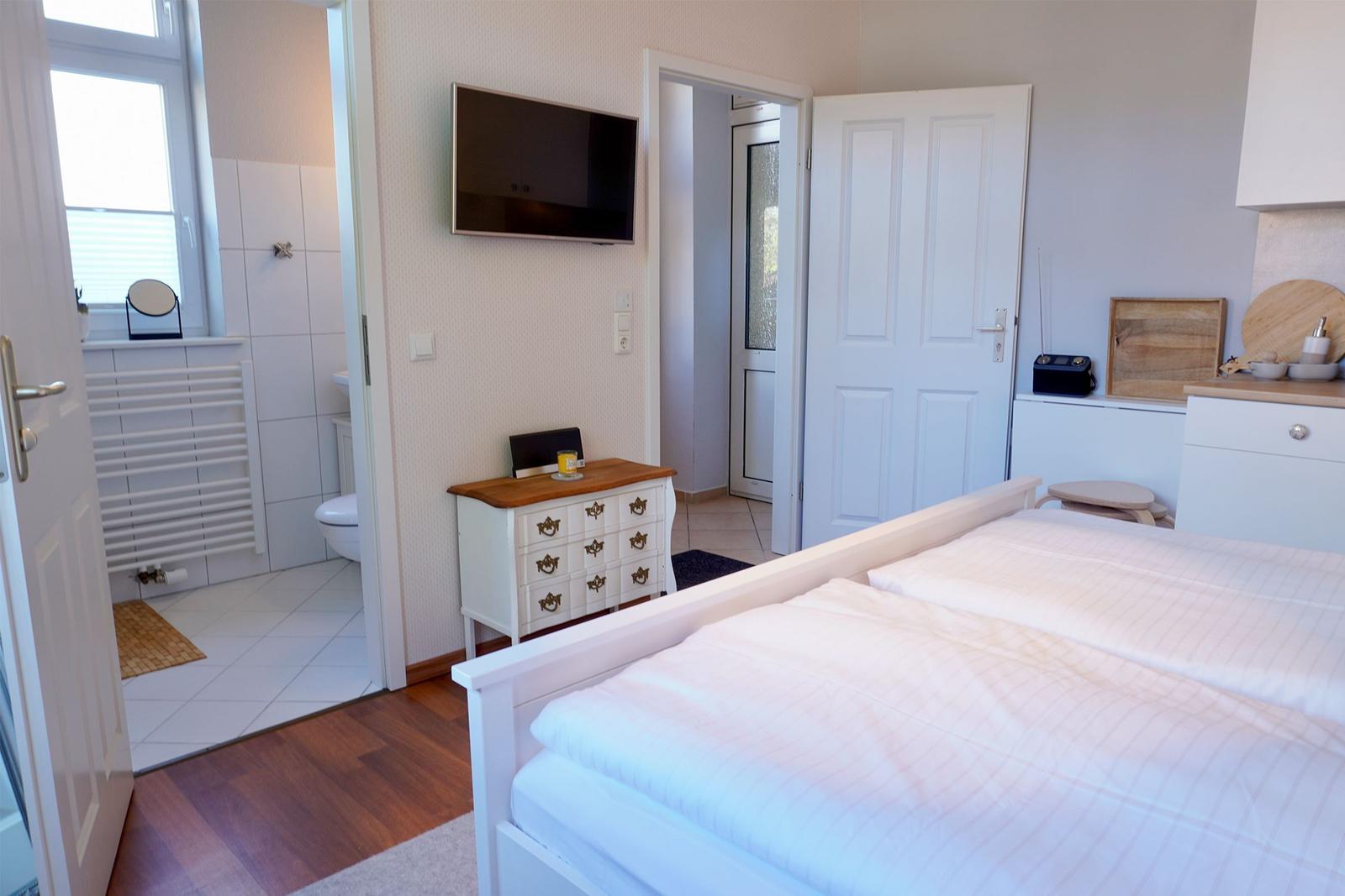 Schlafzimmer mit Doppelbett, Fernseher und Anschluss zur Badewanne.