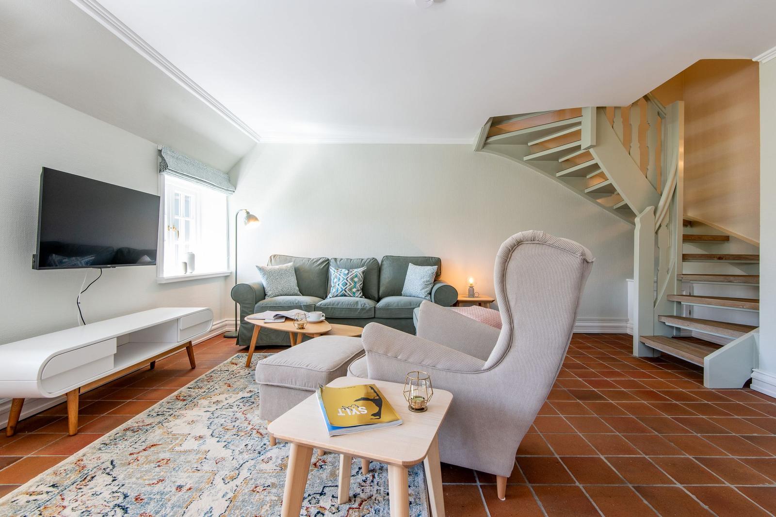 Living room with sofa, armchair, TV, and staircase.