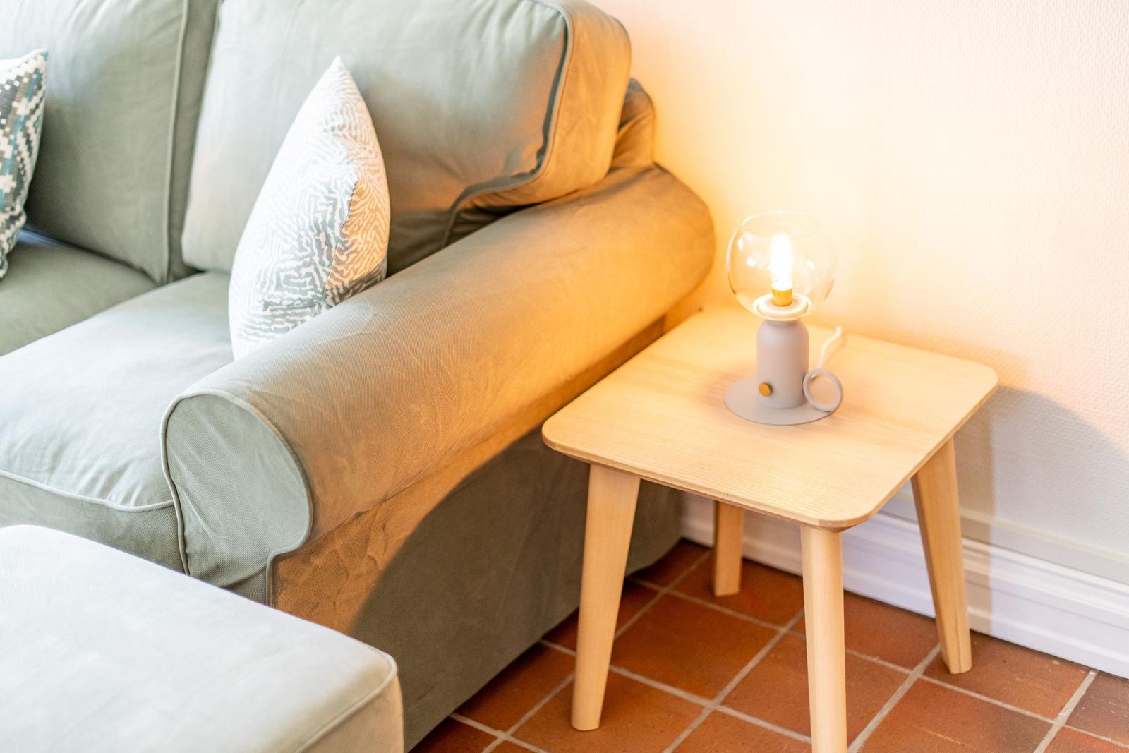 A sofa with cushions and a small table with a lamp.