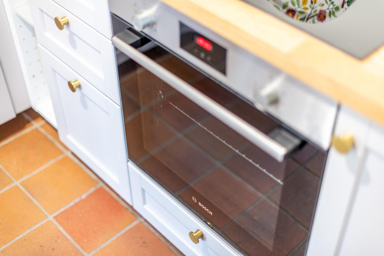 An integrated oven with glass door and control panel in a kitchen with white cabinets and wooden countertop.