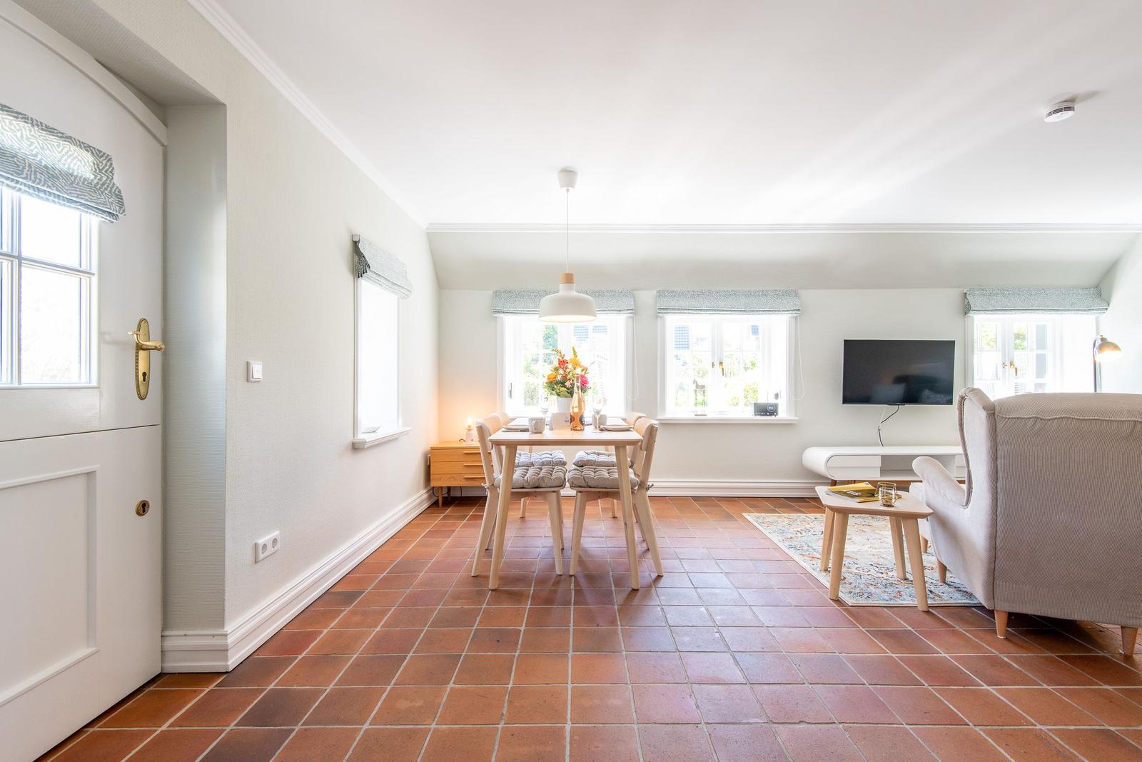 Dining area with table, chairs, and windows. Living area with sofa and TV.