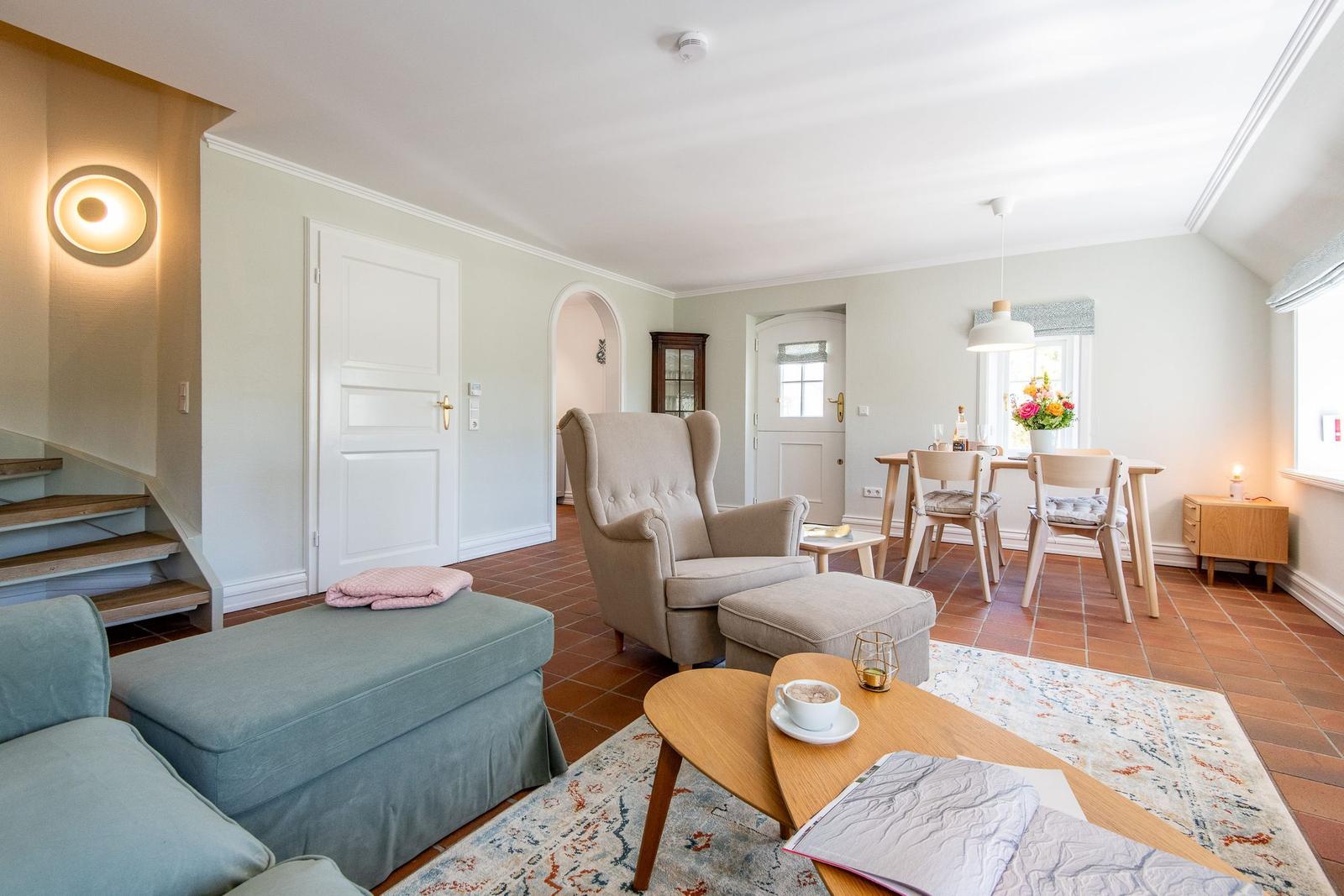 Living and dining area with seating, table and chairs. Wooden staircase and terracotta floor.