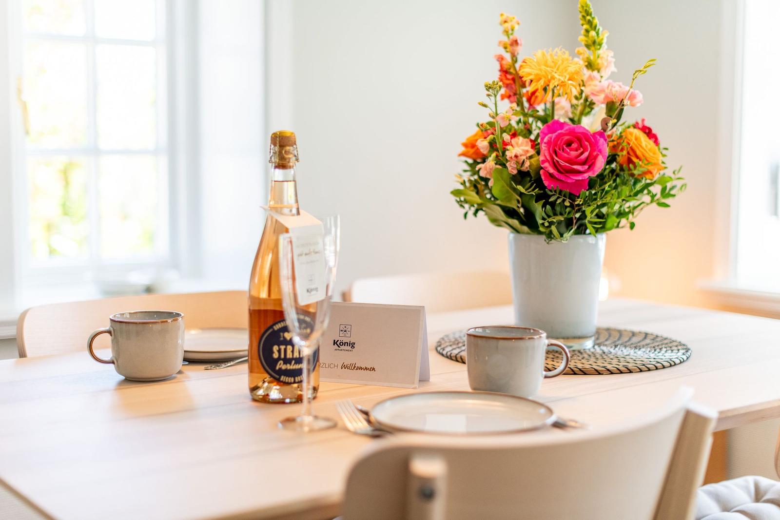 Table with flowers, bottle, and glasses for two people.