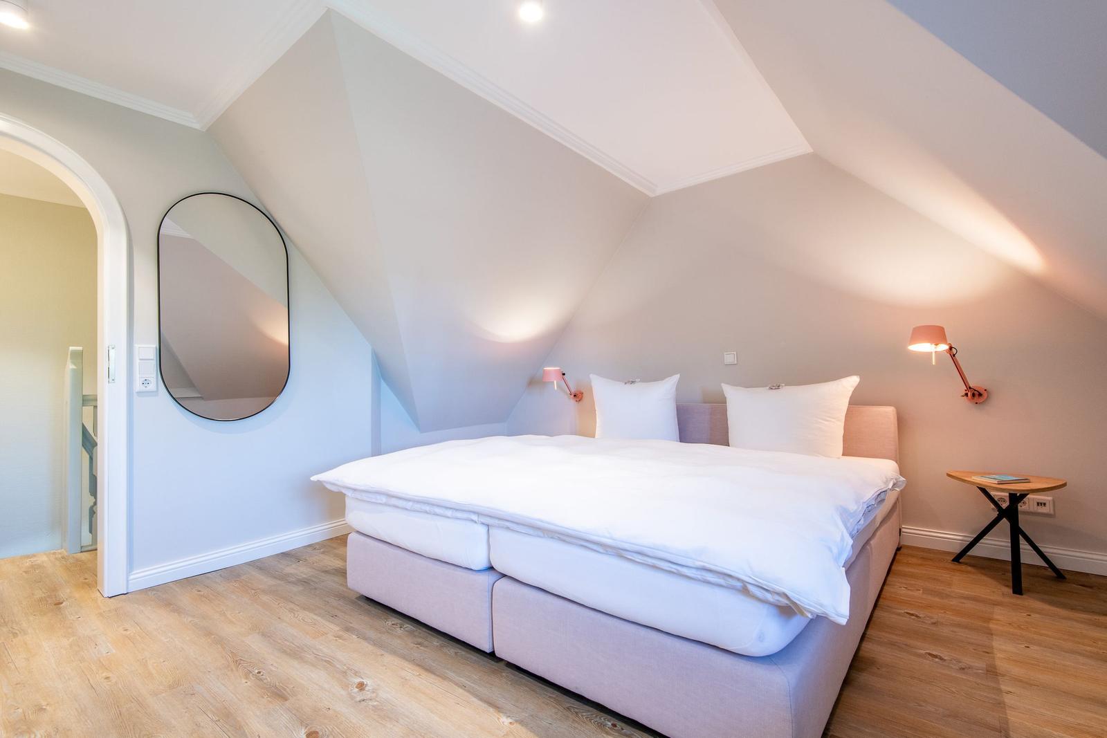 Bedroom with sloped ceiling, bed, wall mirror, and nightstand.