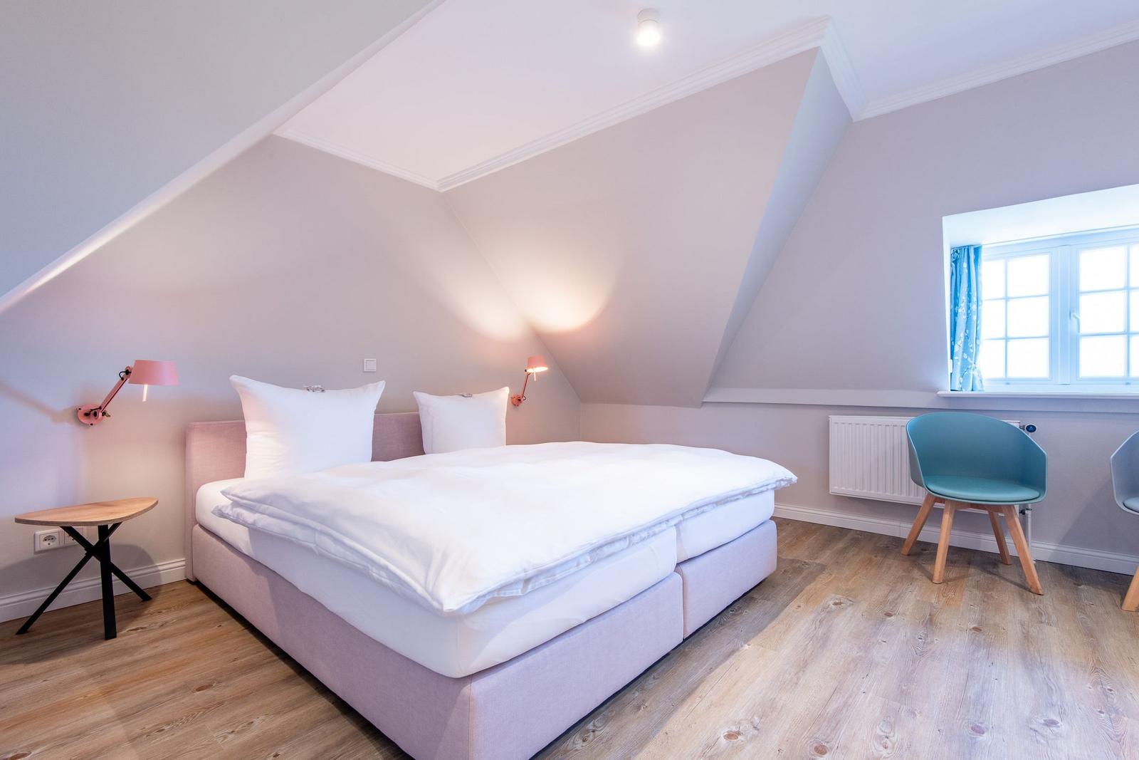 Bedroom with sloped ceiling, bed, chair, and window.